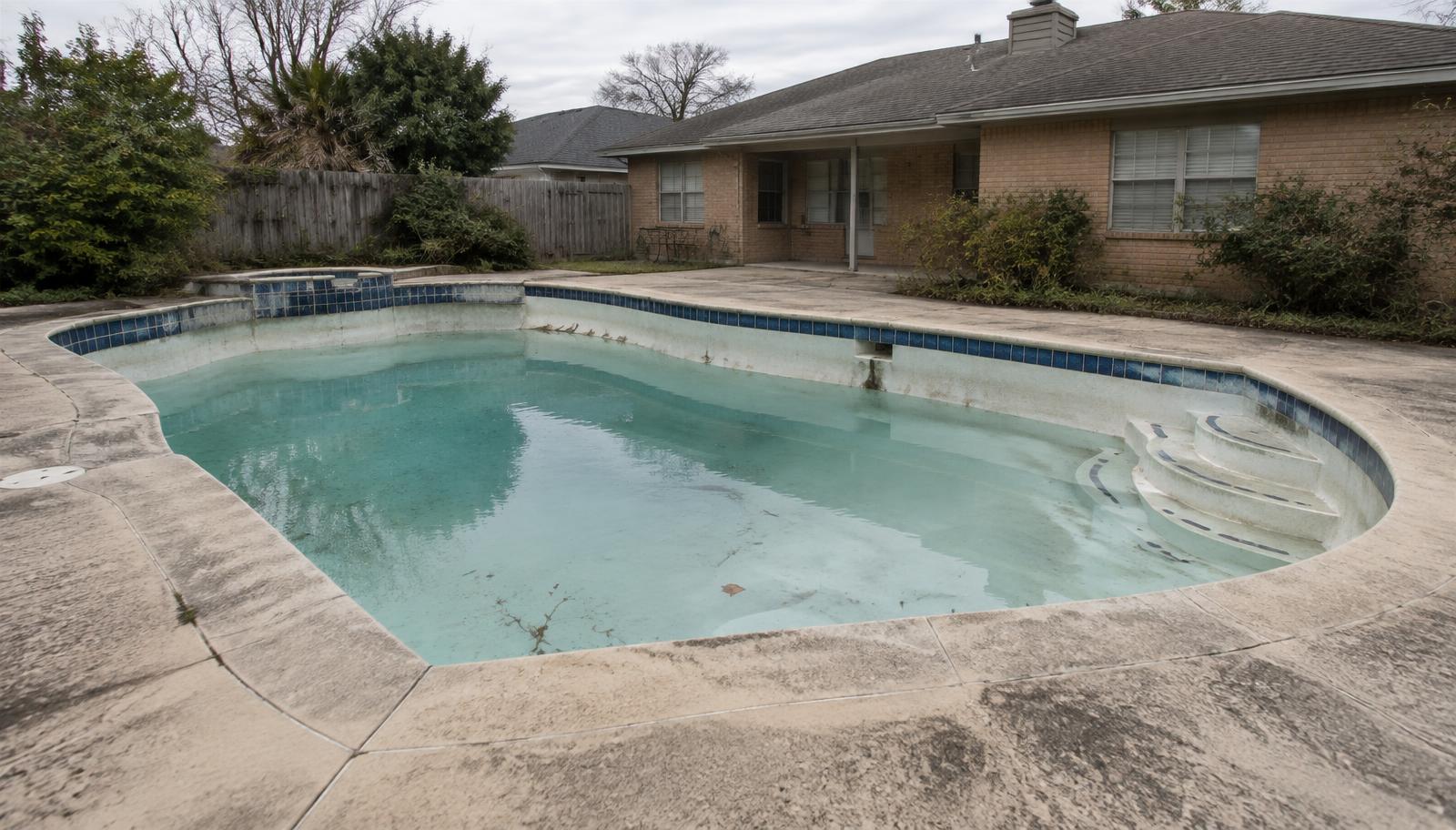 Aging backyard pool with worn finishes before remodeling